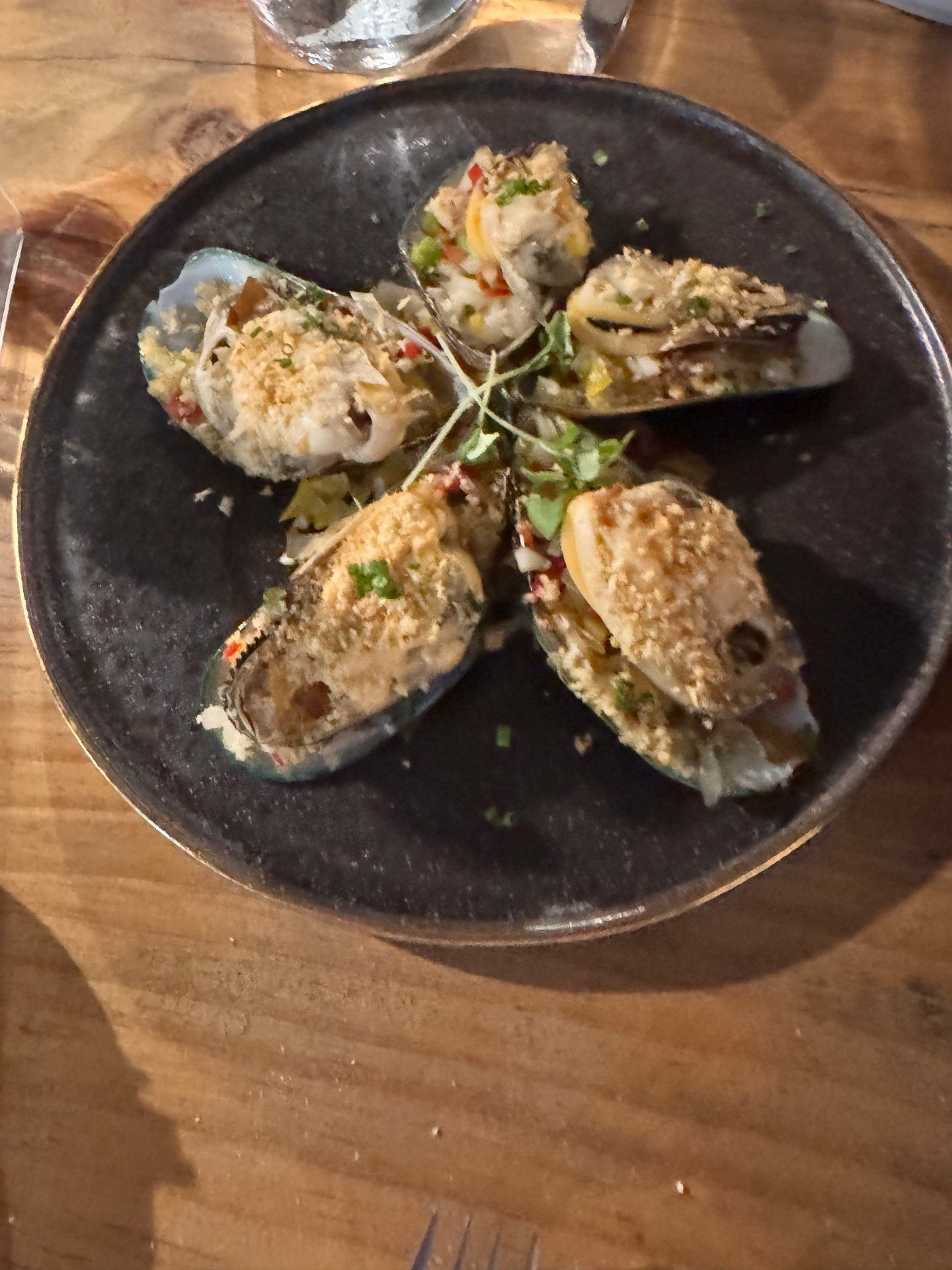 Baked mussels gratin with herbs served on a black ceramic plate at Terra Food Concept in Funchal, Madeira