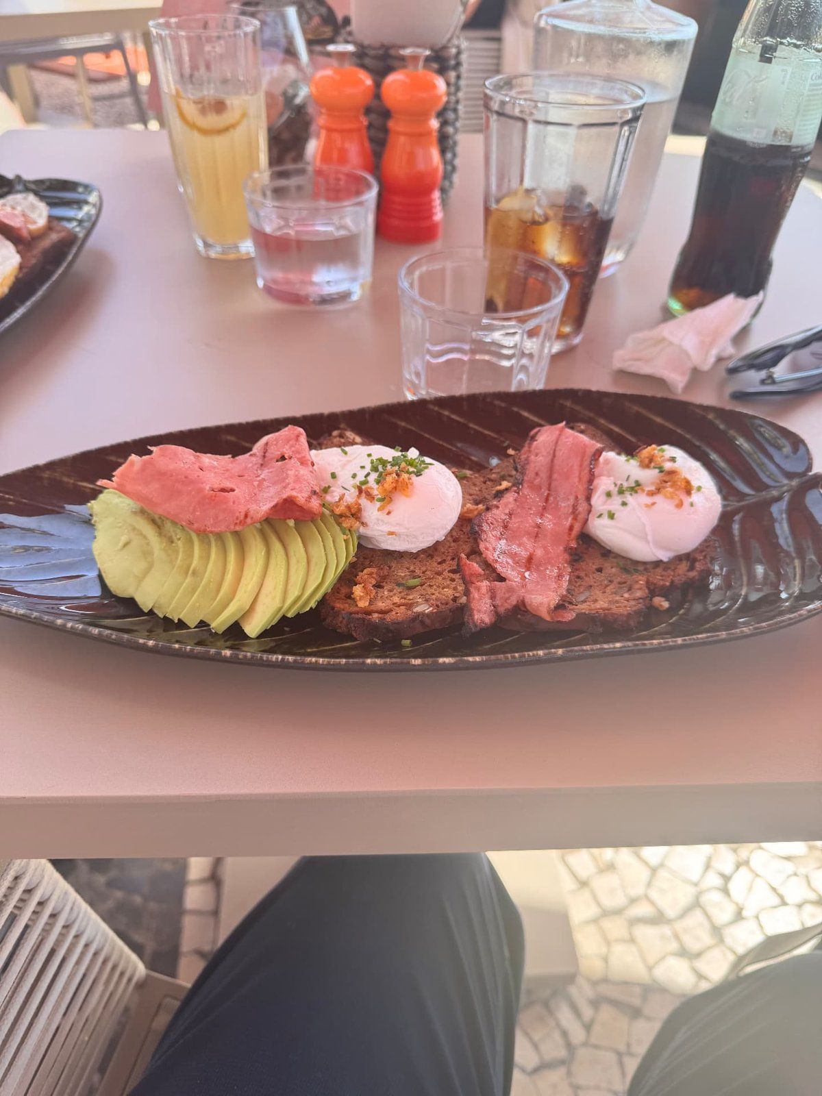 Brunch at Three House restaurant, Funchal - poached eggs with crispy bacon, sliced avocado and toasted bread on a dark ceramic plate