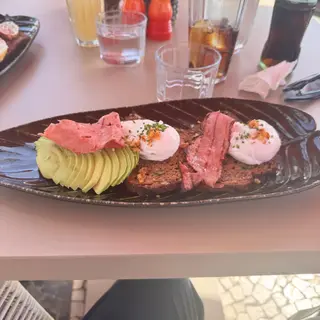 Brunch at Three House restaurant, Funchal - poached eggs with crispy bacon, sliced avocado and toasted bread on a dark ceramic plate