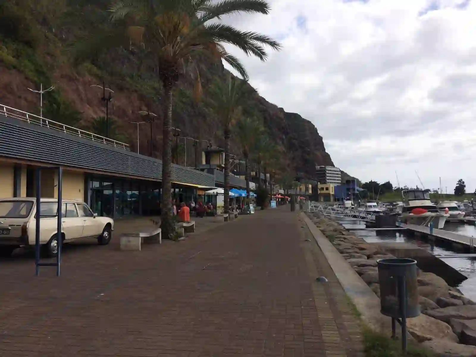 Passeio ladeado por palmeiras na marina da Calheta, com cafés e restaurantes ao pé da falésia