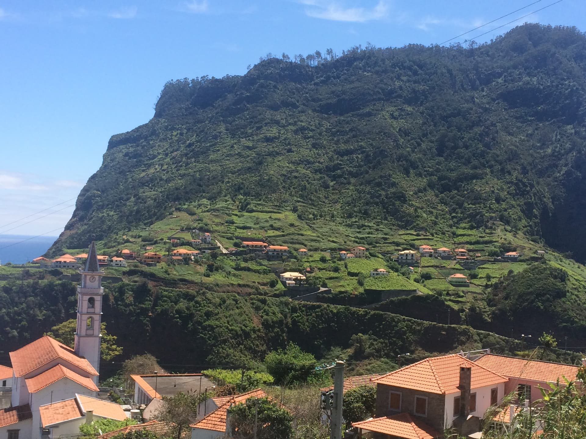 Faial church tower beneath the steep green mountain and terraced fields, Madeira north coast