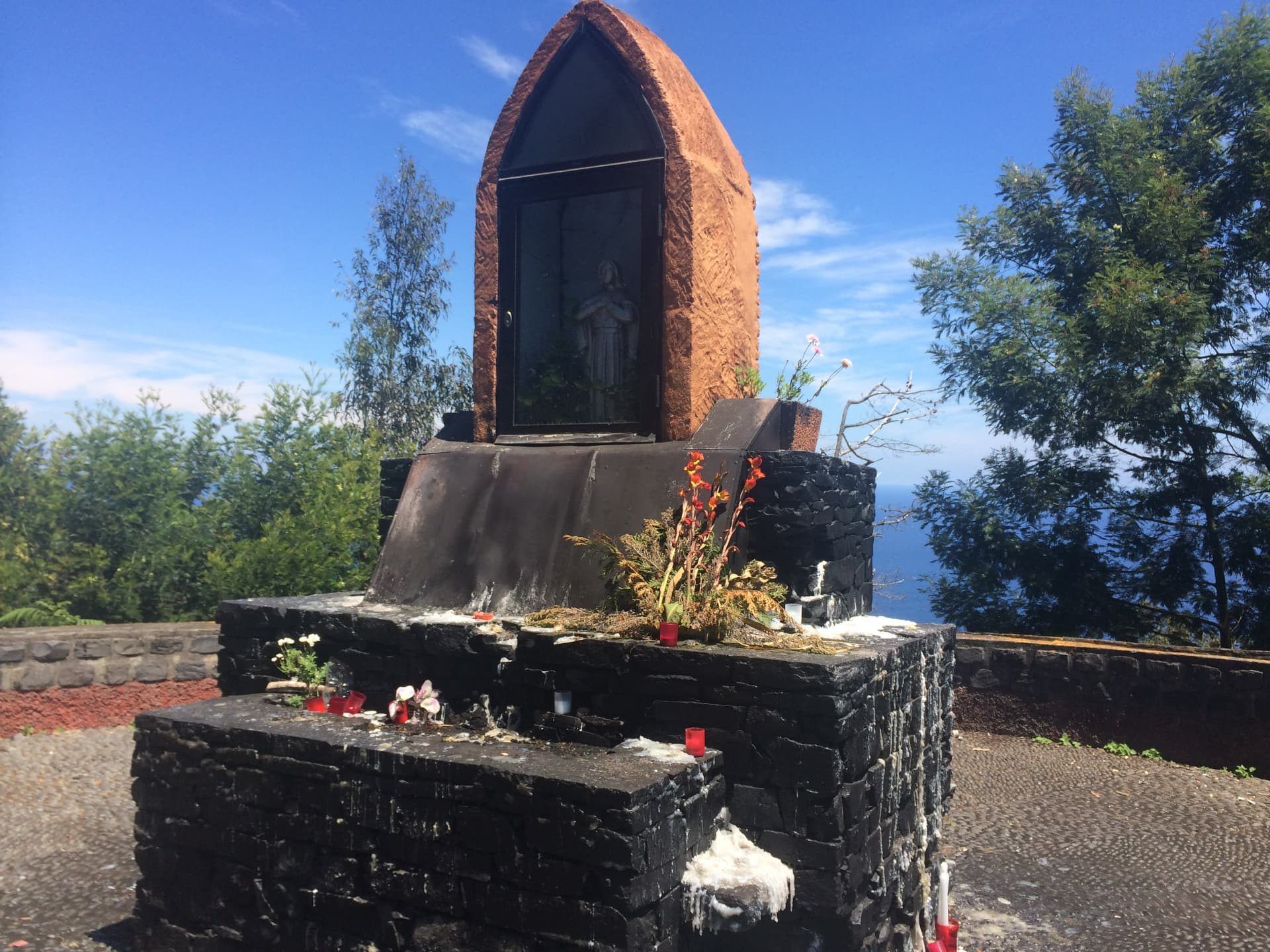 Um santuário de pedra à beira da estrada, com velas e flores, com vista para o Atlântico, no Faial, na Madeira