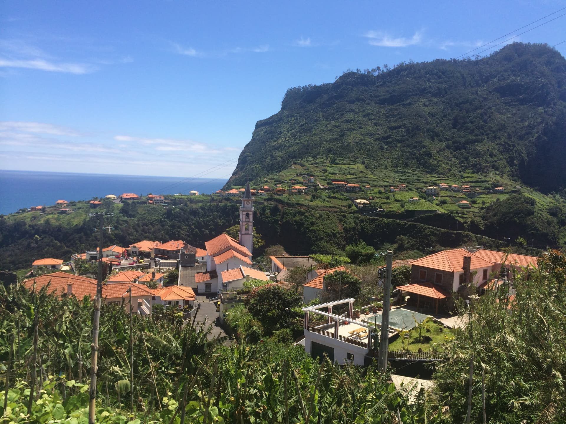 Faial village church tower and red rooftops below the forested cliffs of Penha d Agua, with the Atlantic behind