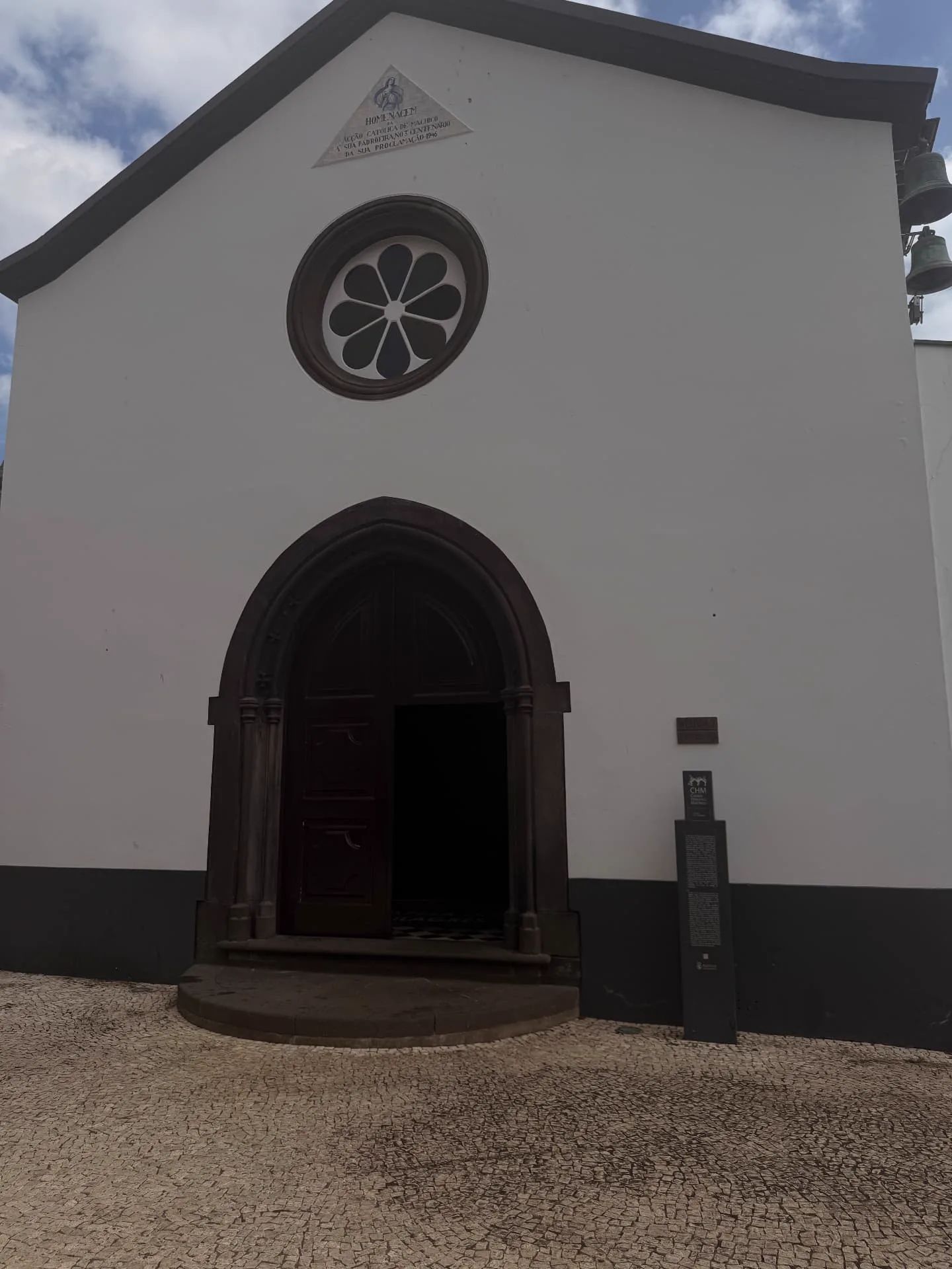Fachada de uma capela branca em Machico, com um portal gótico em pedra escura, uma janela circular e uma torre sineira.