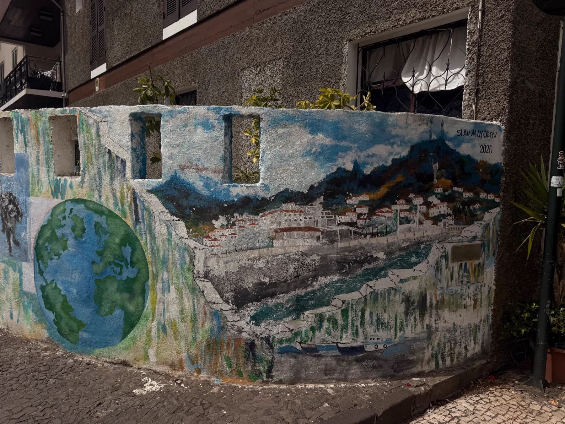 Mural pintado representando a baía de Machico e o globo terrestre numa parede junto a uma rua de calçada em Machico.