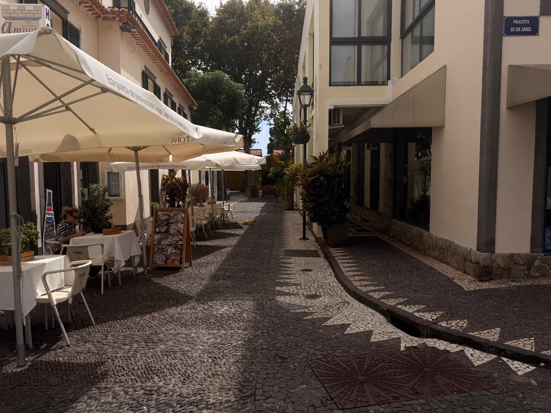 Esplanada de um restaurante e rua de calçada com padrões na Praceta 25 de Abril, no centro de Machico.