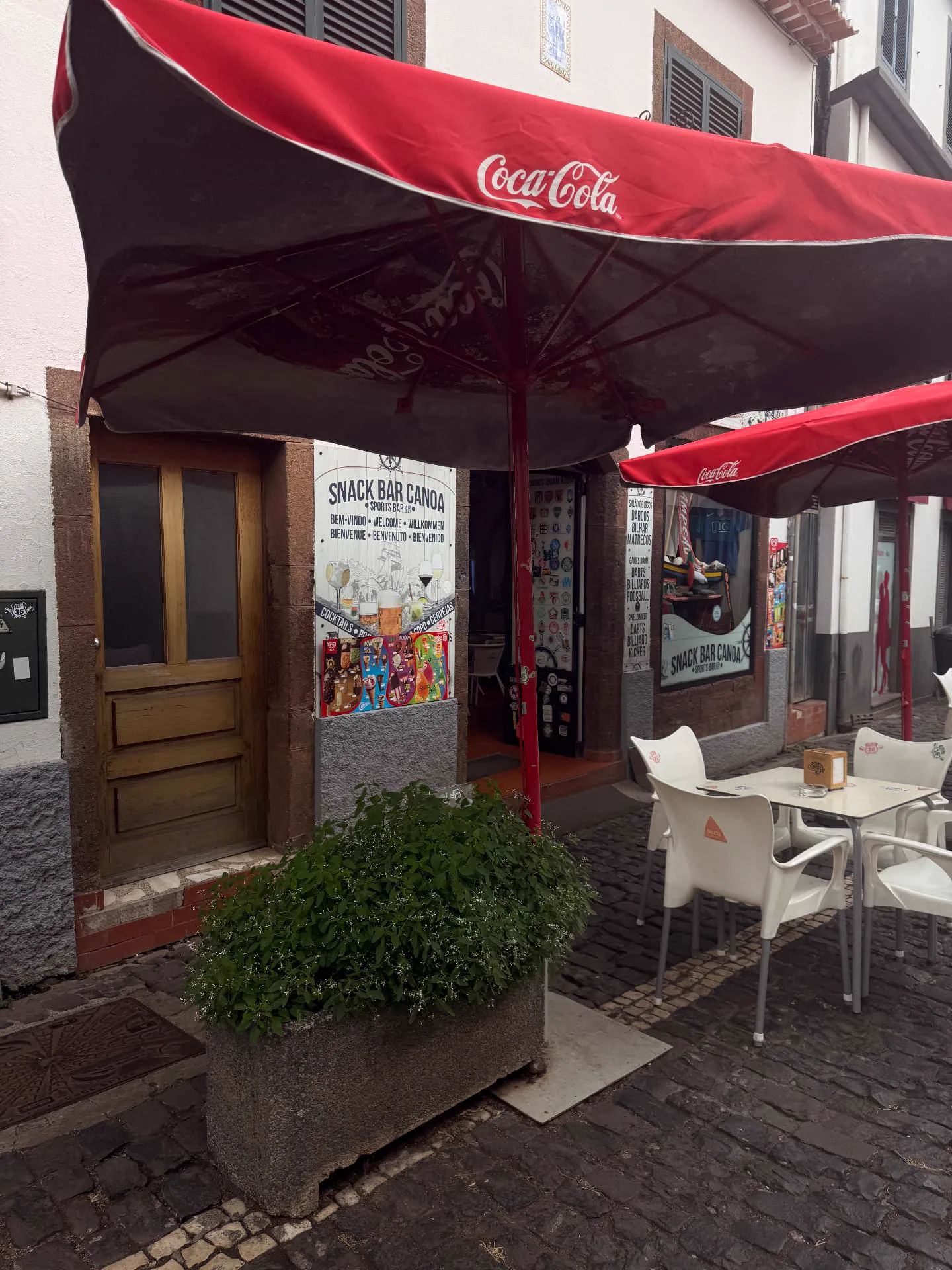 Snack Bar Canoa in Machico with red umbrellas and outdoor tables on the cobbled street.