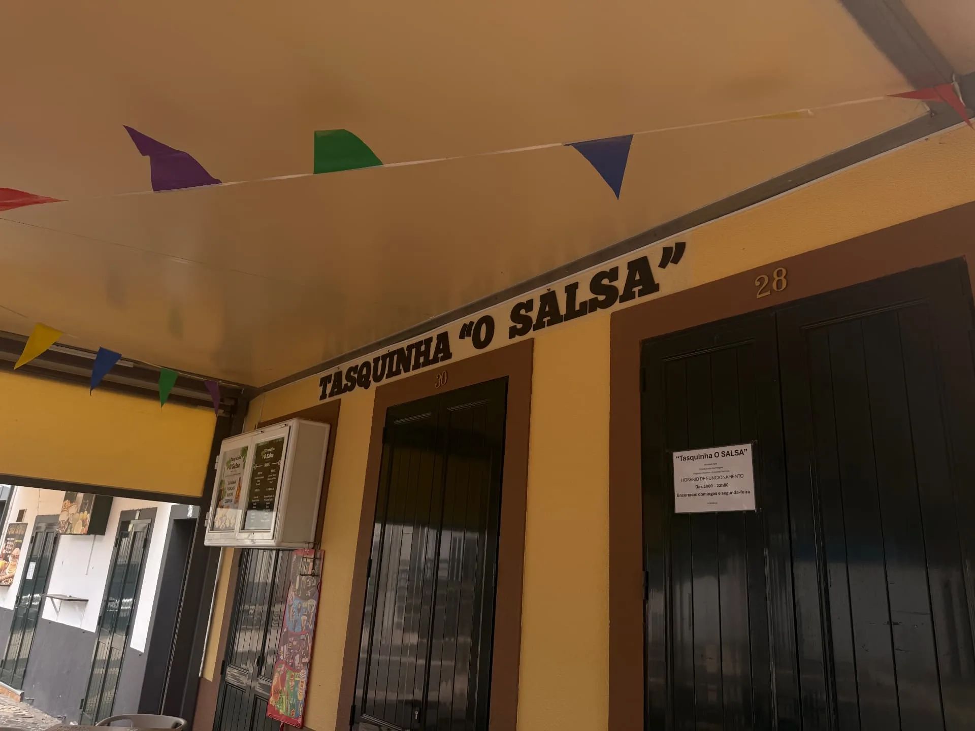 Fachada do restaurante Tasquinha «O Salsa», em Machico, com letreiro pintado e aviso do horário de funcionamento na porta