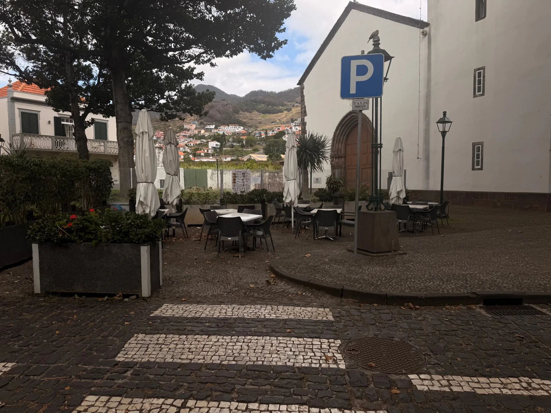 Mesas de café ao ar livre junto à igreja de Machico, com vista para as colinas