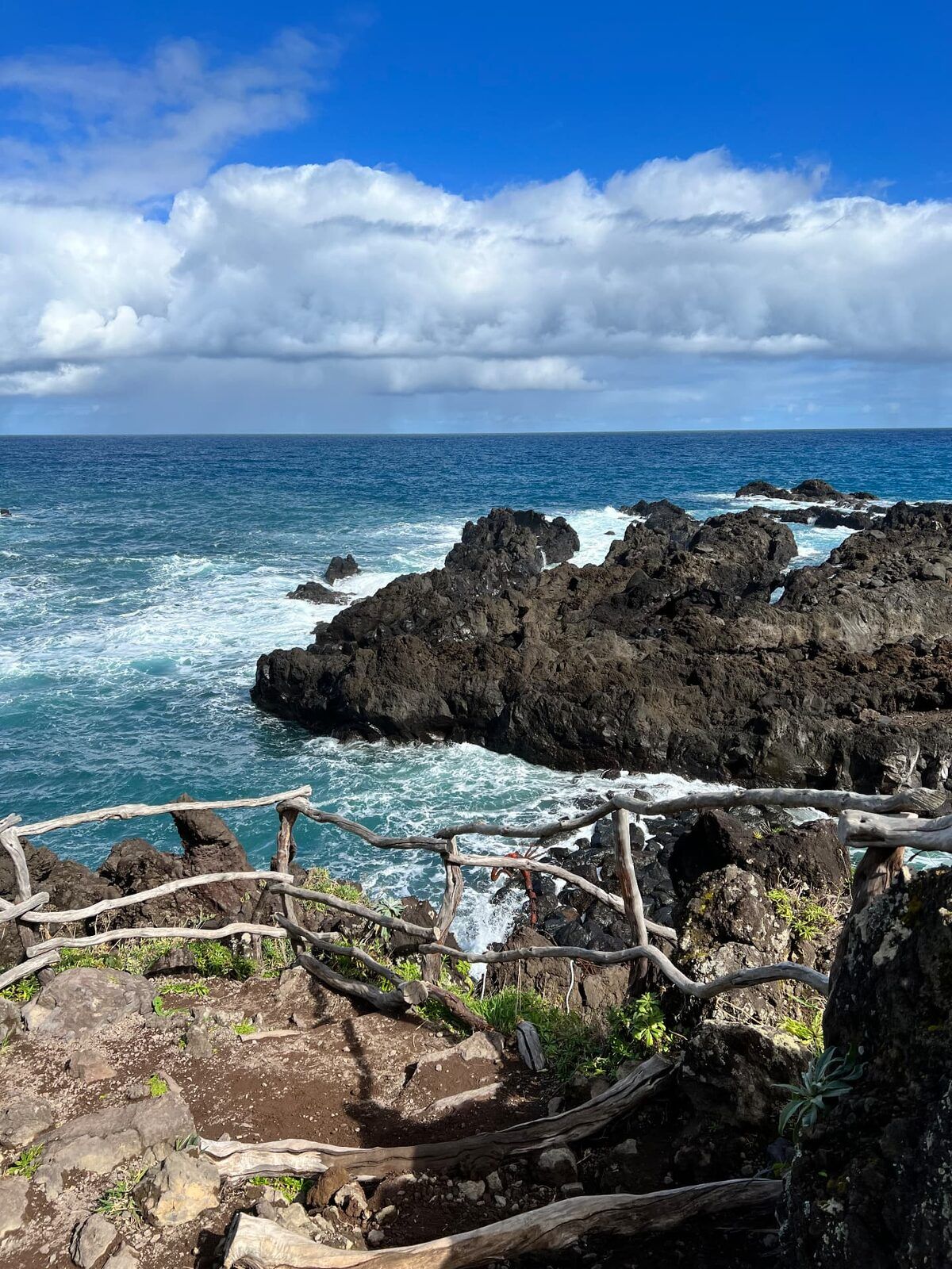 Rocha vulcânica negra e ondas do Atlântico a rebentar por trás de uma cerca rústica de madeira em Porto Moniz