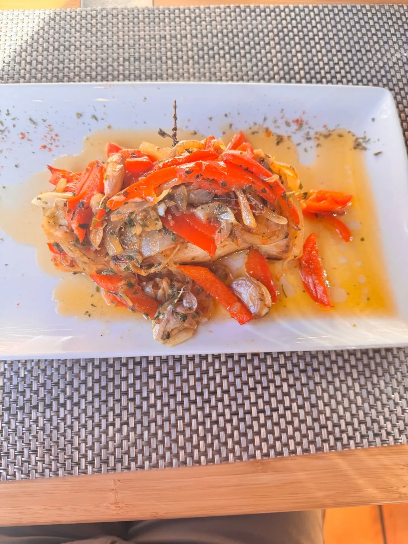 Filete de peixe coberto com pimentos vermelhos, cebola e alho num restaurante de Santana