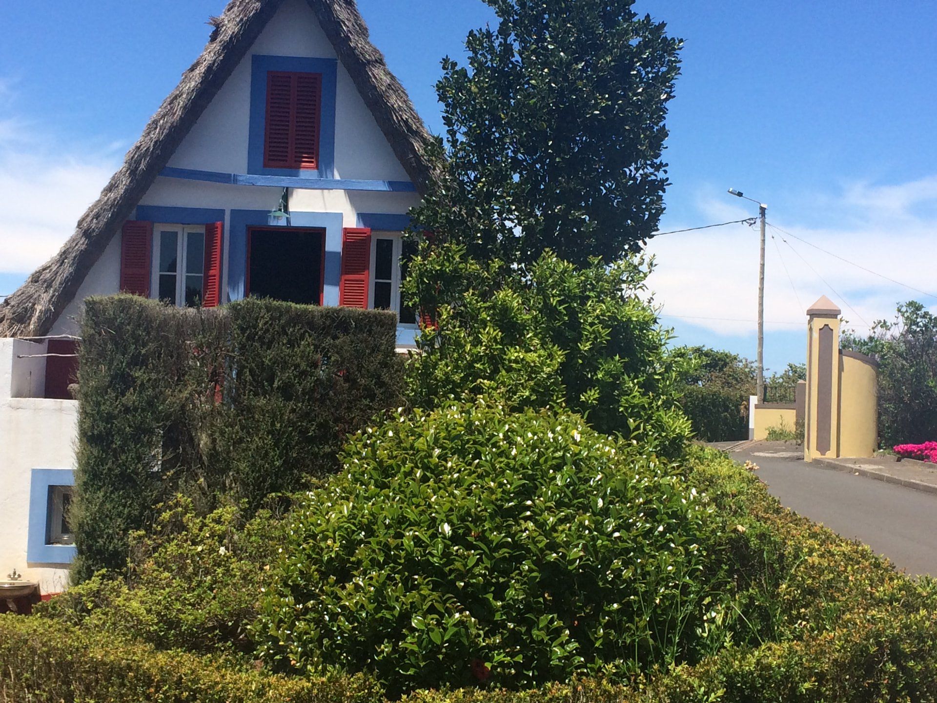 Casa de Santana com telhado de colmo e persianas vermelhas, por trás de sebes bem aparadas