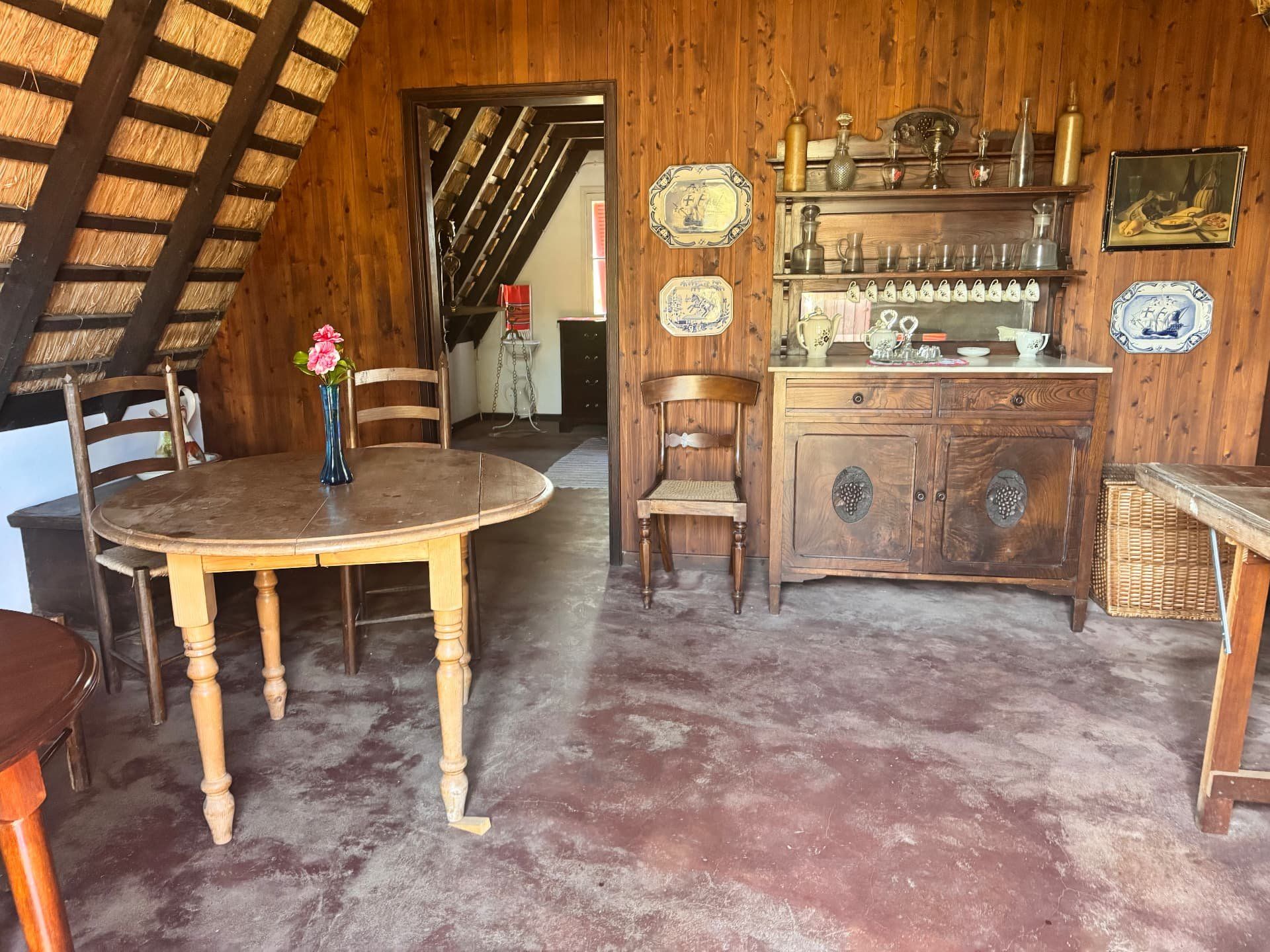 Sala de jantar no interior de uma casa tradicional de Santana com telhado de colmo, com uma mesa redonda de pinho e paredes revestidas a painéis de madeira