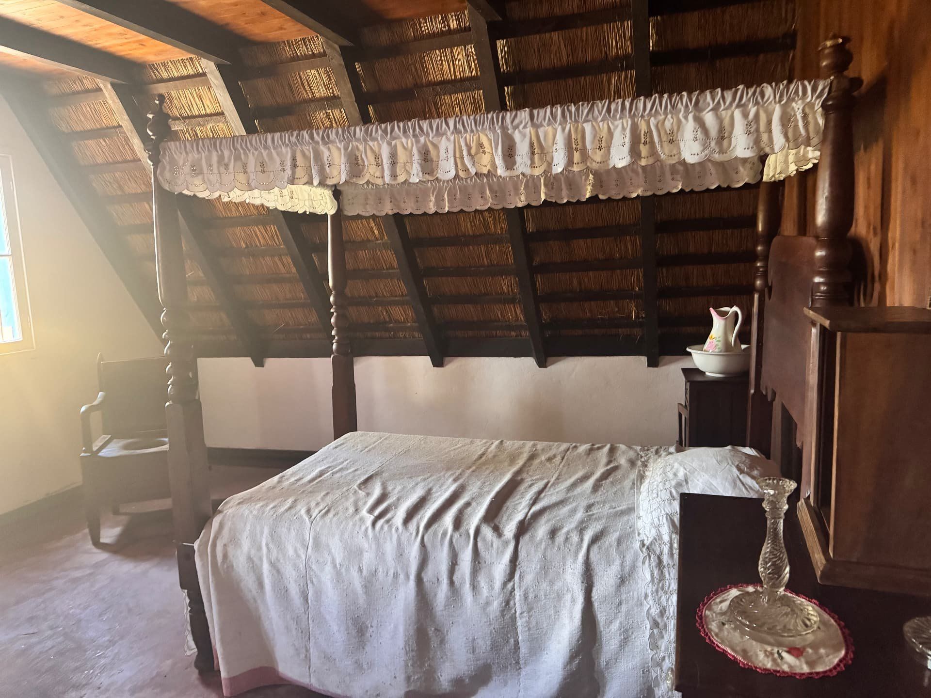Cama de dossel esculpida com dossel bordado numa casa tradicional de Santana com telhado de colmo
