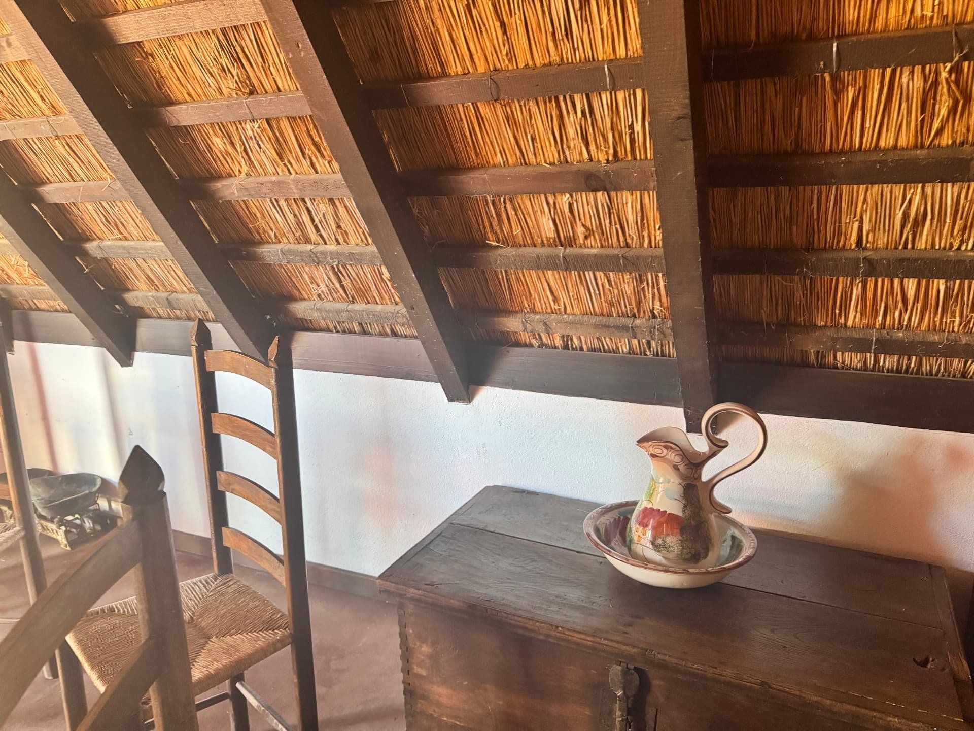 Jarro e bacia pintados sobre um baú de madeira, sob o telhado de colmo de uma casa de Santana