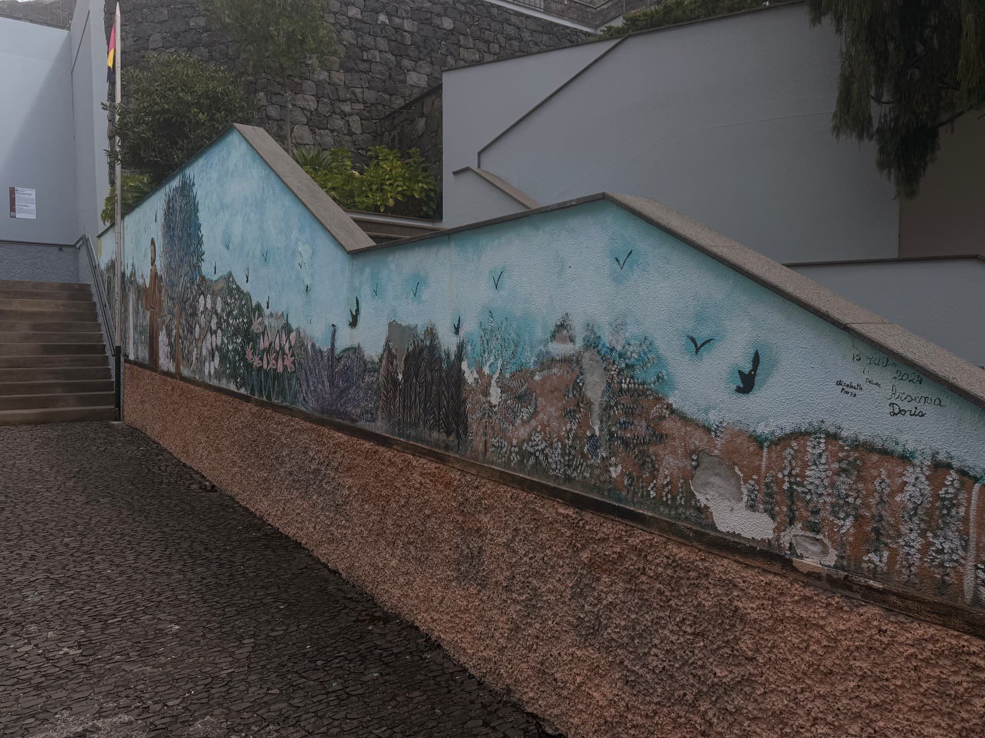 Longa parede pintada com flores, árvores e pássaros junto a um caminho de calçada e escadas no Curral das Freiras