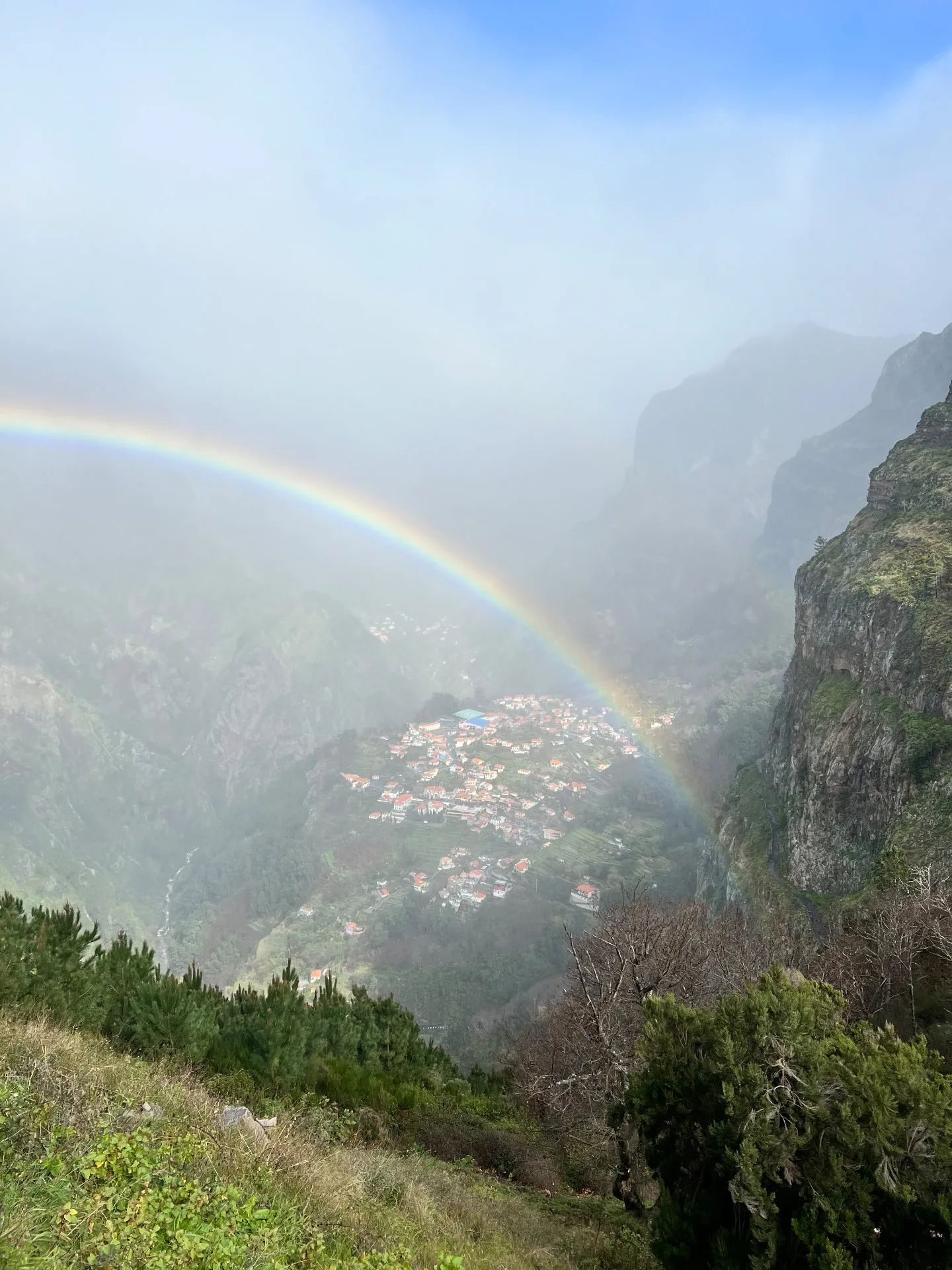 Rainbow over Curral das Freiras, the village seen from high above in its valley between steep cliffs and mist