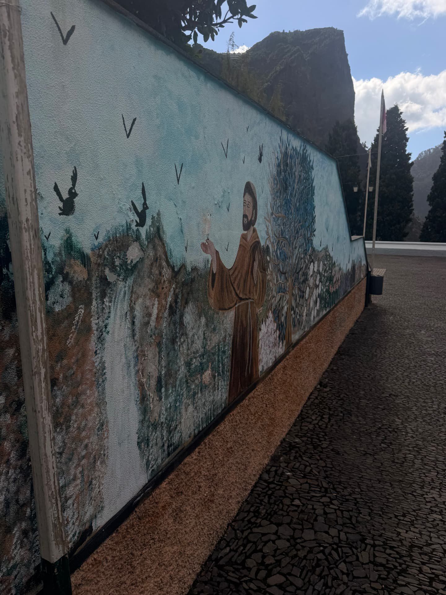 Mural pintado de São Francisco com pássaros, flores e uma cascata numa parede do Curral das Freiras
