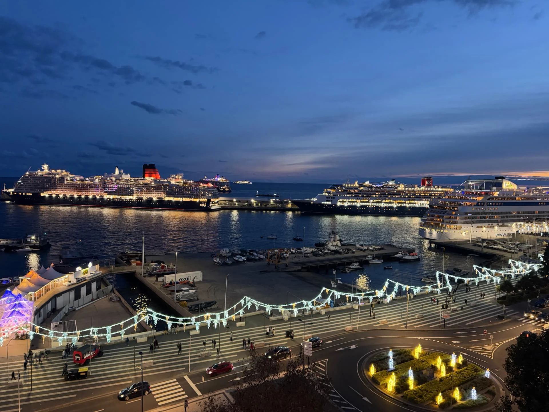 Several cruise ships moored in Funchal bay at dusk with festive Christmas lights on the waterfront promenade, Madeira