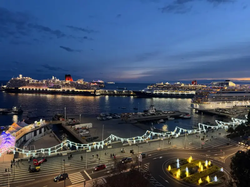 Several cruise ships moored in Funchal bay at dusk with festive Christmas lights on the waterfront promenade, Madeira
