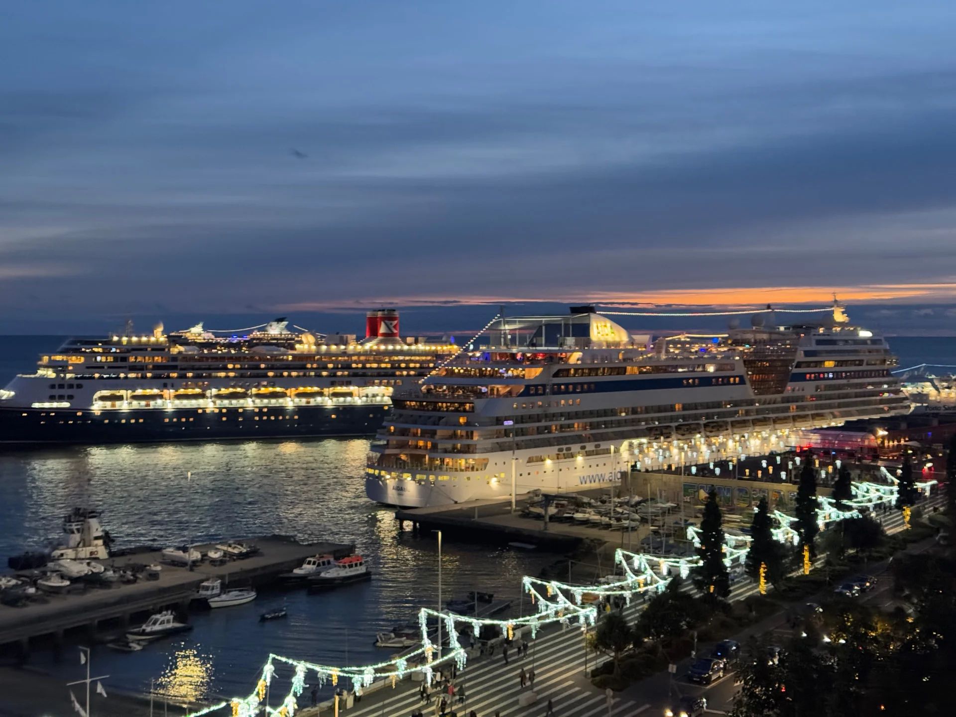 Cruise ships Queen Victoria and AIDAstella lit up at dusk in Funchal harbour with Christmas lights along the seafront, Madeira