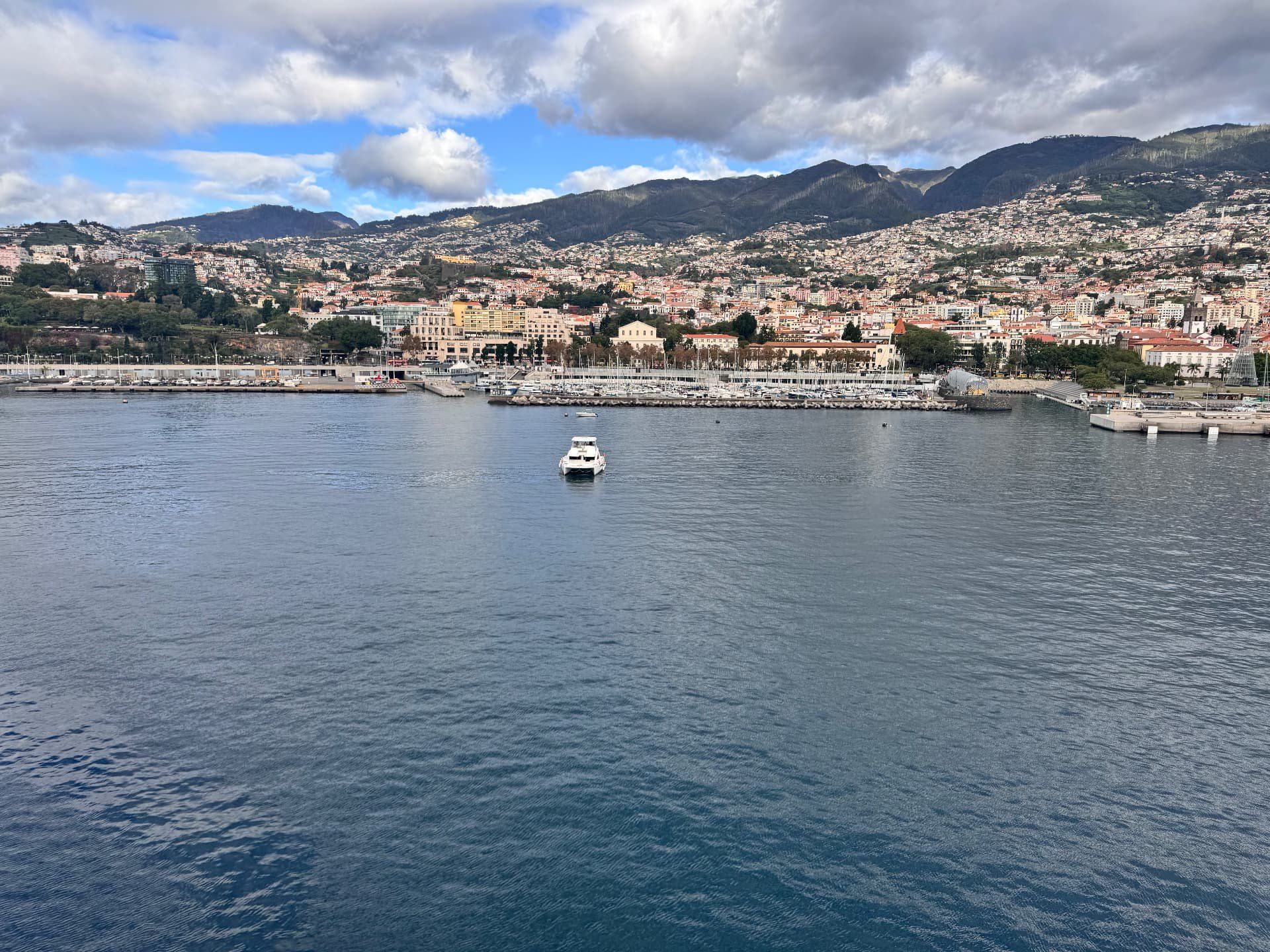 A boat entering Funchal harbour with the city and mountains of Madeira behind