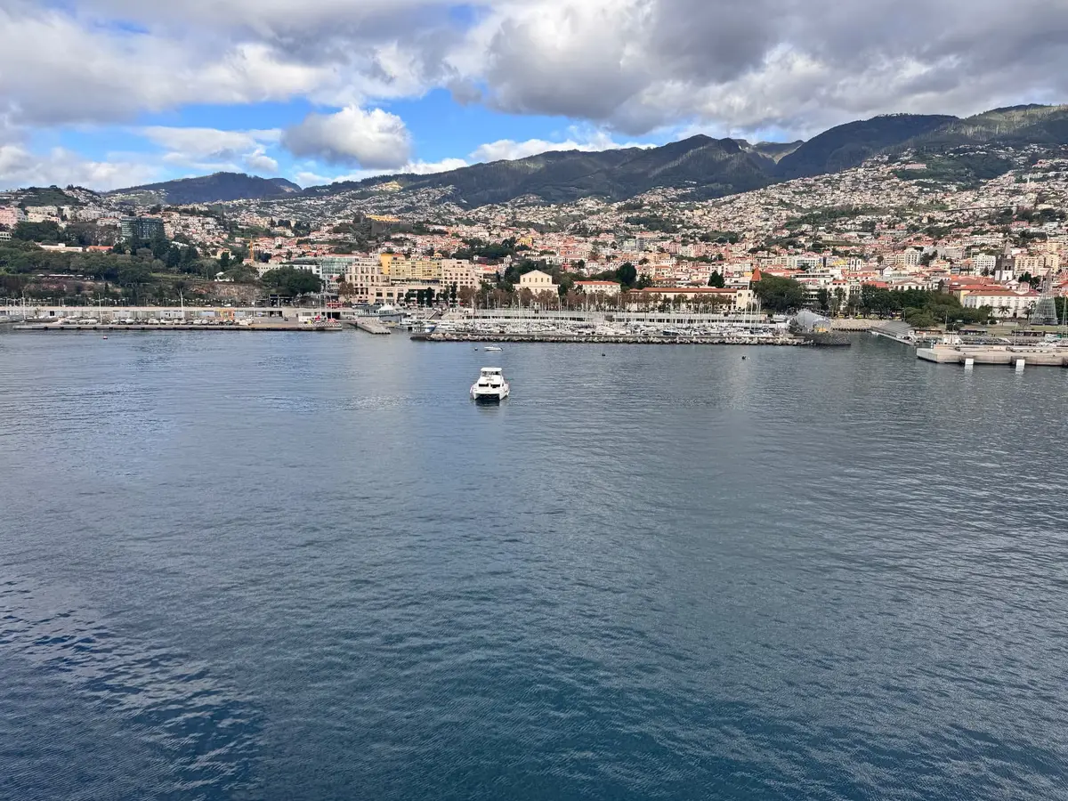A boat entering Funchal harbour with the city and mountains of Madeira behind