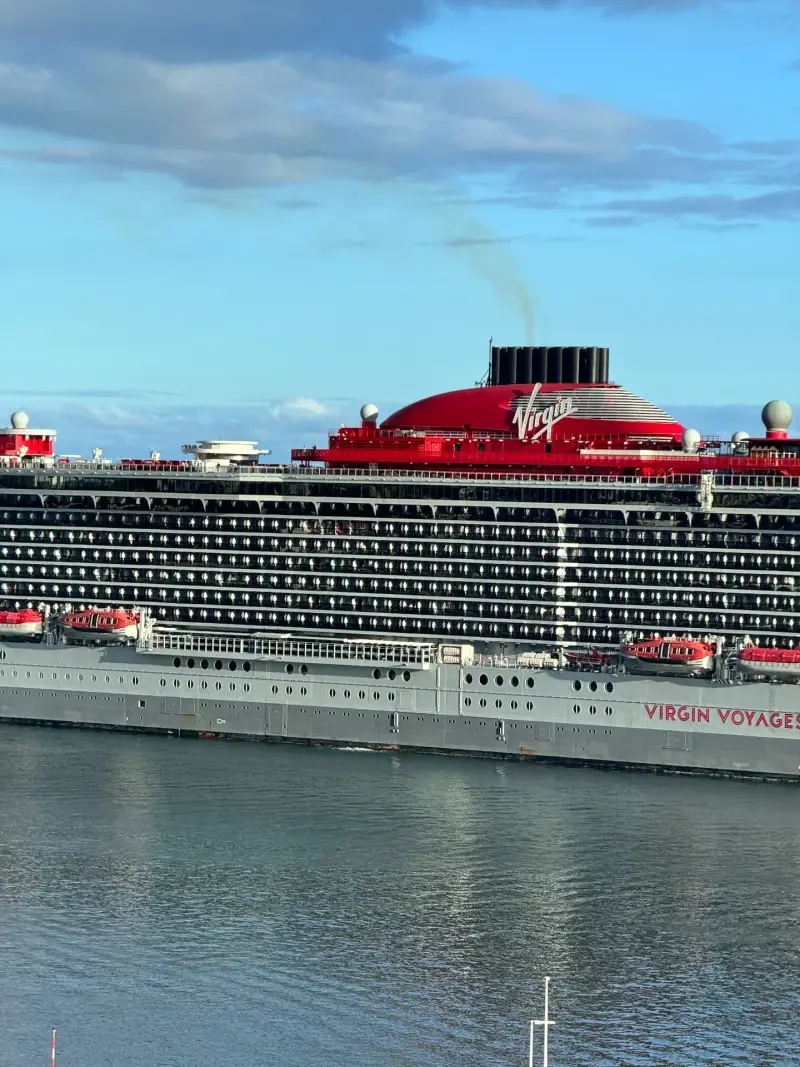 Close-up of the red funnel and upper decks of a Virgin Voyages cruise ship alongside Funchal cruise pier, Madeira