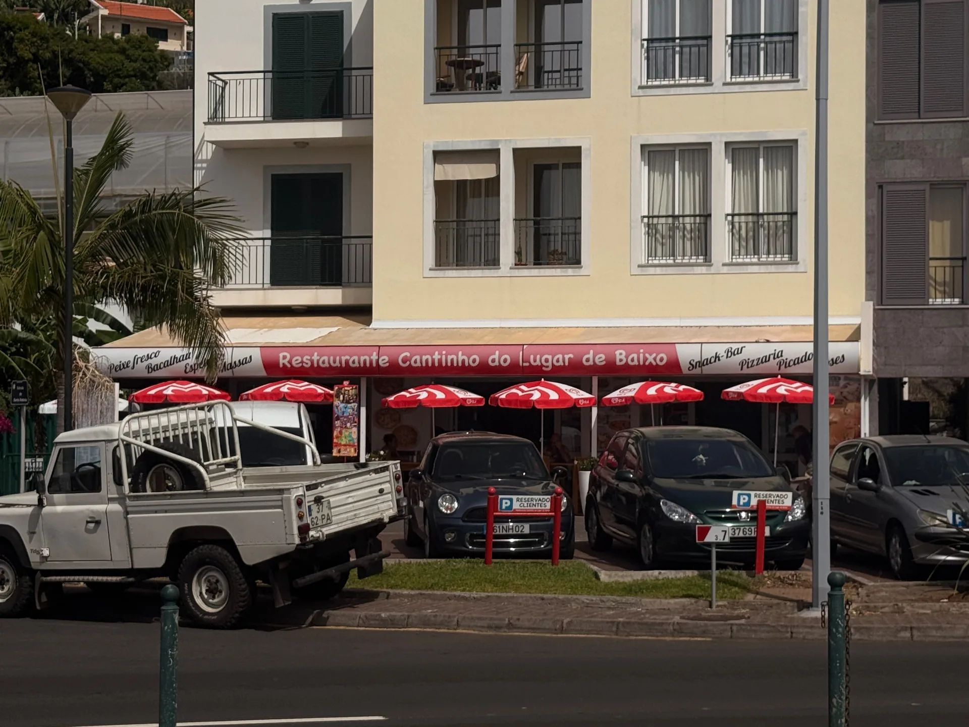 Restaurante Cantinho do Lugar de Baixo with red parasols and signs for fresh fish, bacalhau, espetada, pizza and picado