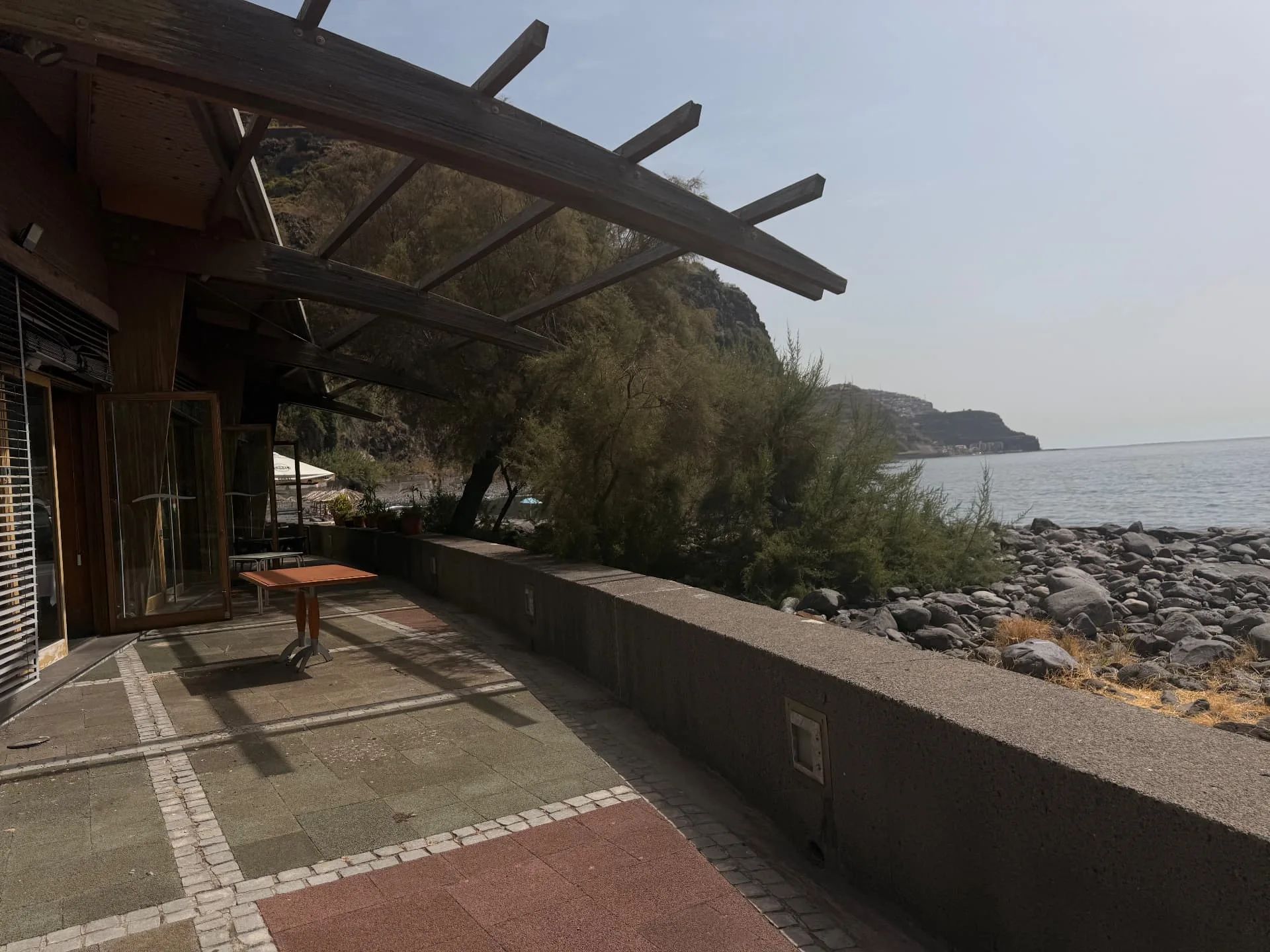 Seafront terrace under a wooden pergola, with boulders, tamarisk trees and the sea at Lugar de Baixo