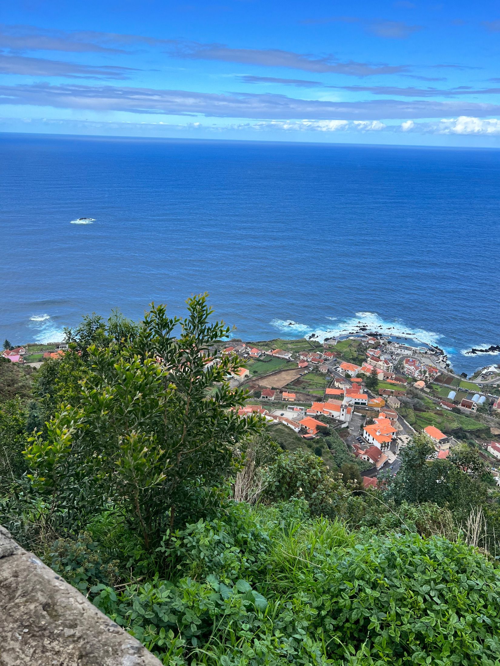 Vista da encosta sobre casas de telhados vermelhos, terrenos cultivados e costa rochosa