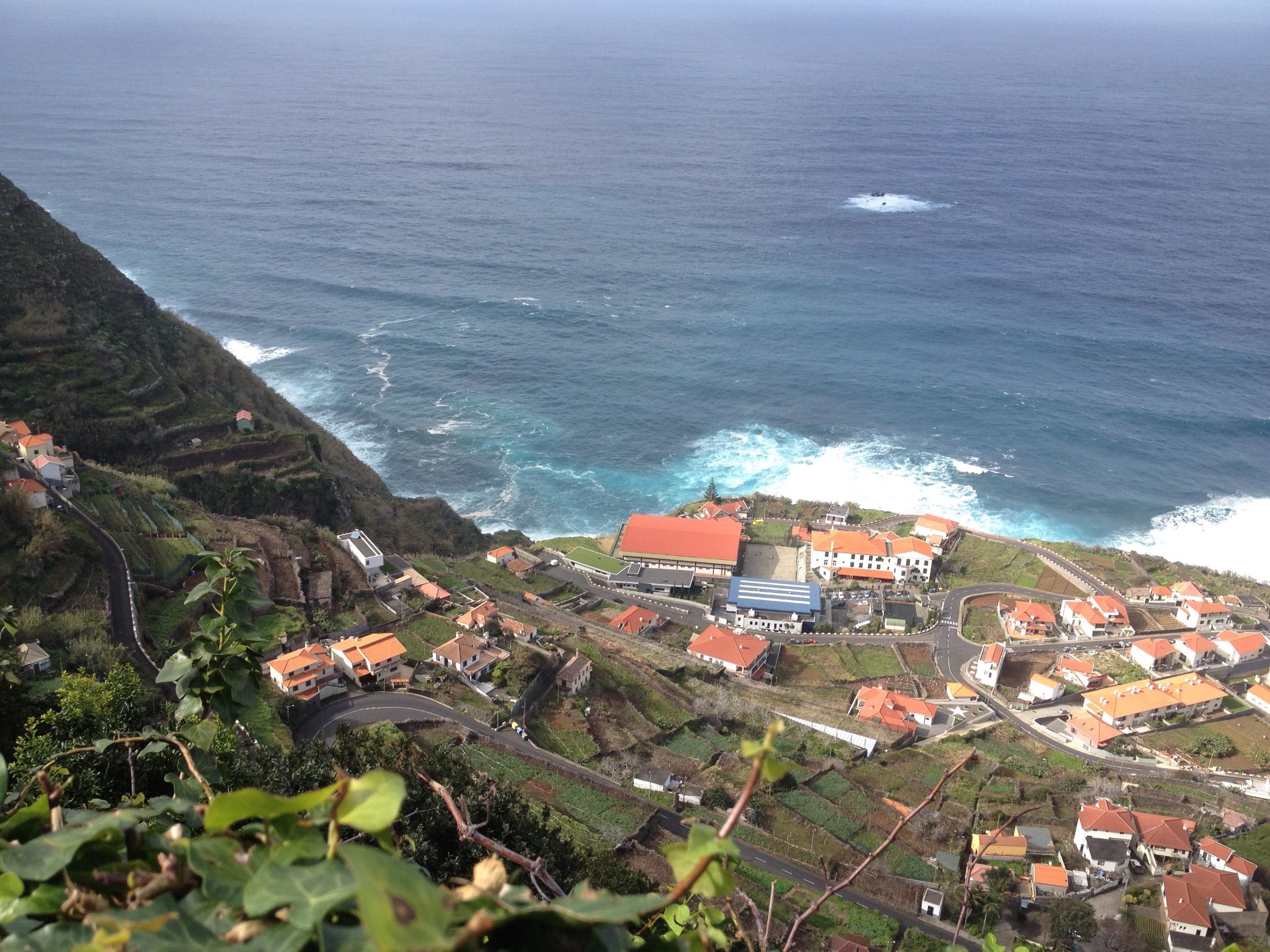 Casas de telhados vermelhos e campos em socalcos junto a estradas sinuosas sobre uma costa rochosa