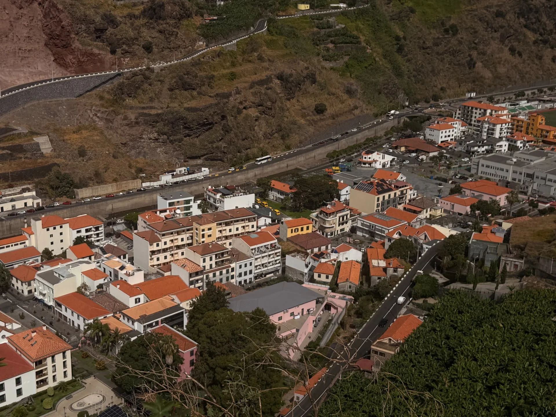 Vista de perto sobre os telhados do centro da cidade da Ribeira Brava, o leito do rio e a estrada sinuosa que sobe pela encosta do vale