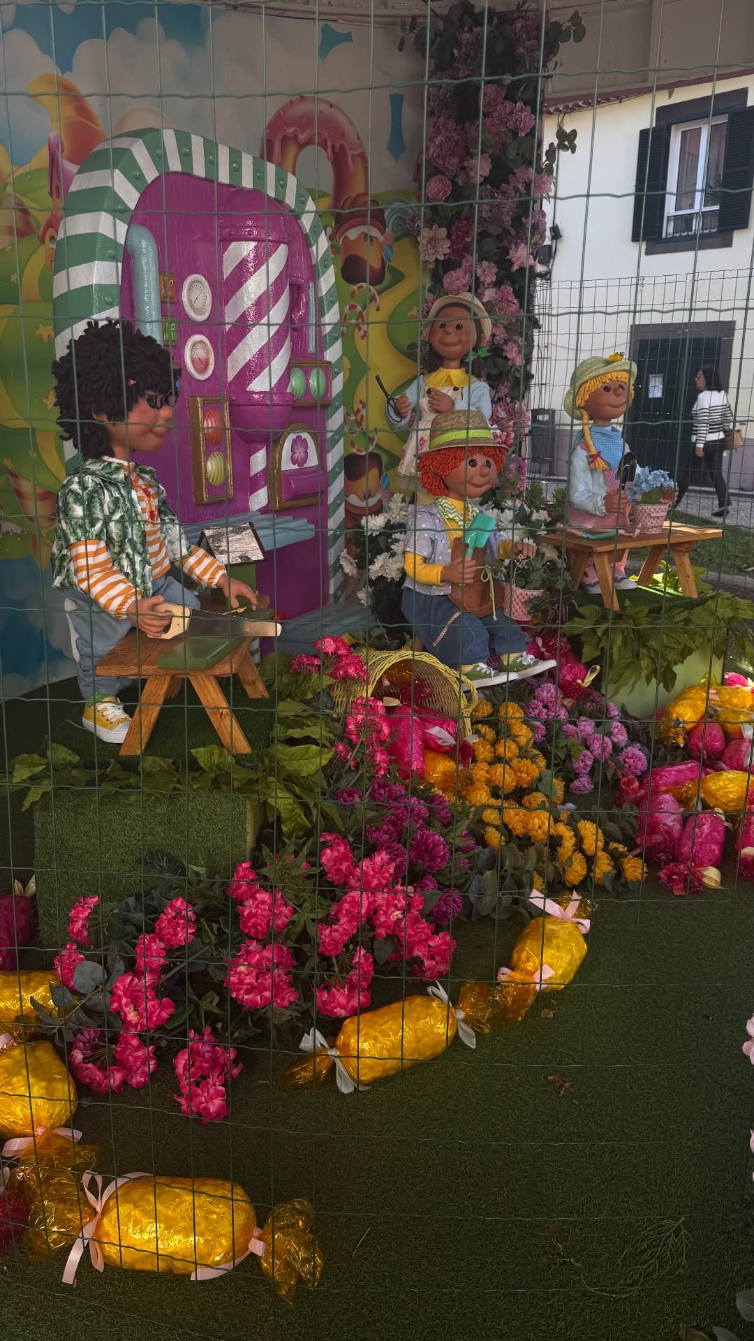 Figuras de crianças a trabalhar entre flores e rebuçados gigantes numa exposição floral em Santa Cruz, Madeira