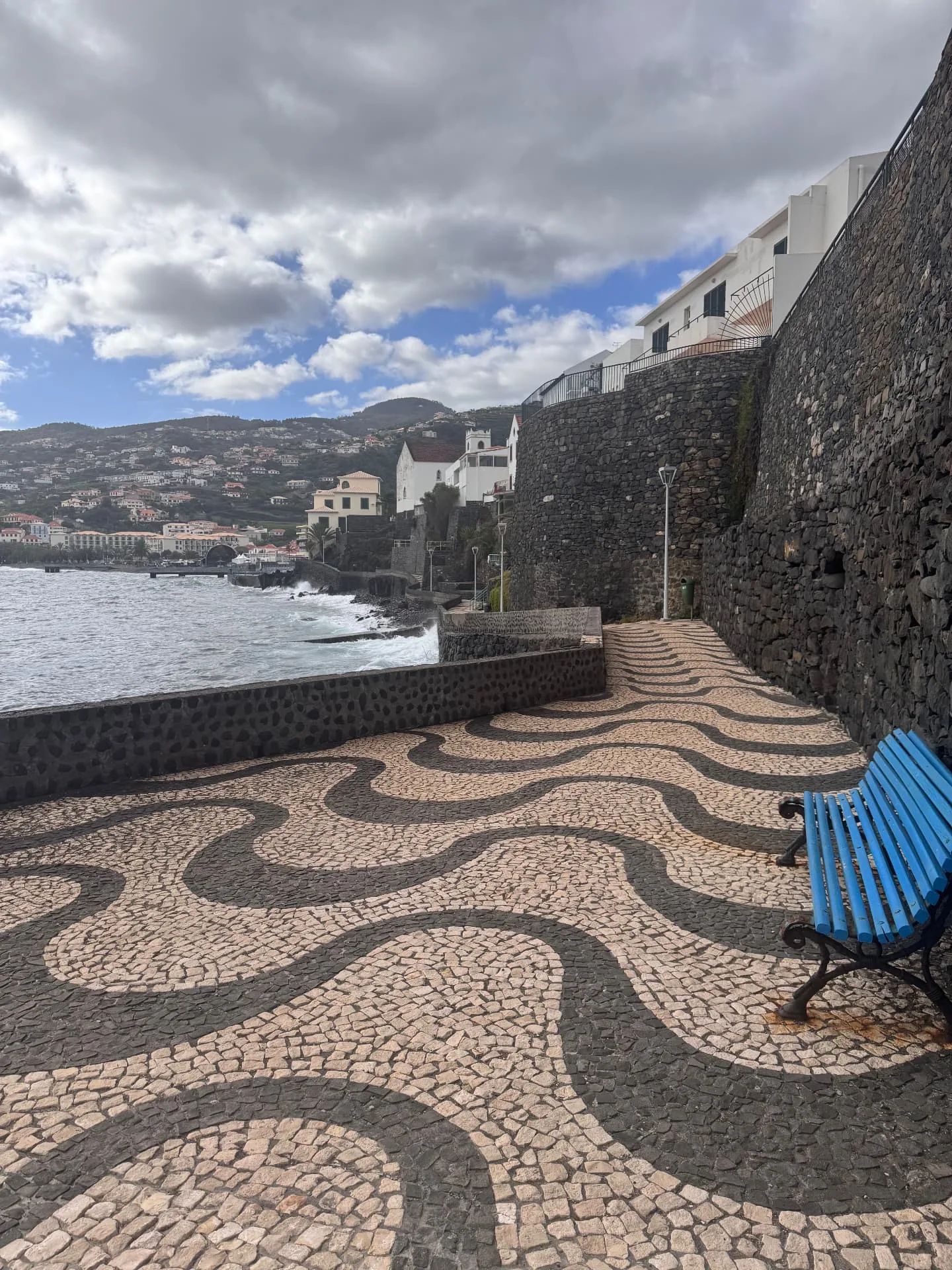 Passeio em calçada com padrão de ondas e banco azul junto à muralha em Santa Cruz