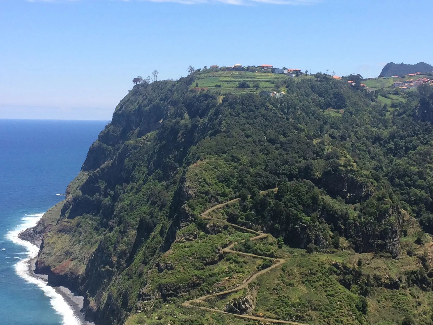 Steep green coastal cliffs at São Jorge falling to the Atlantic, an old path zigzagging down