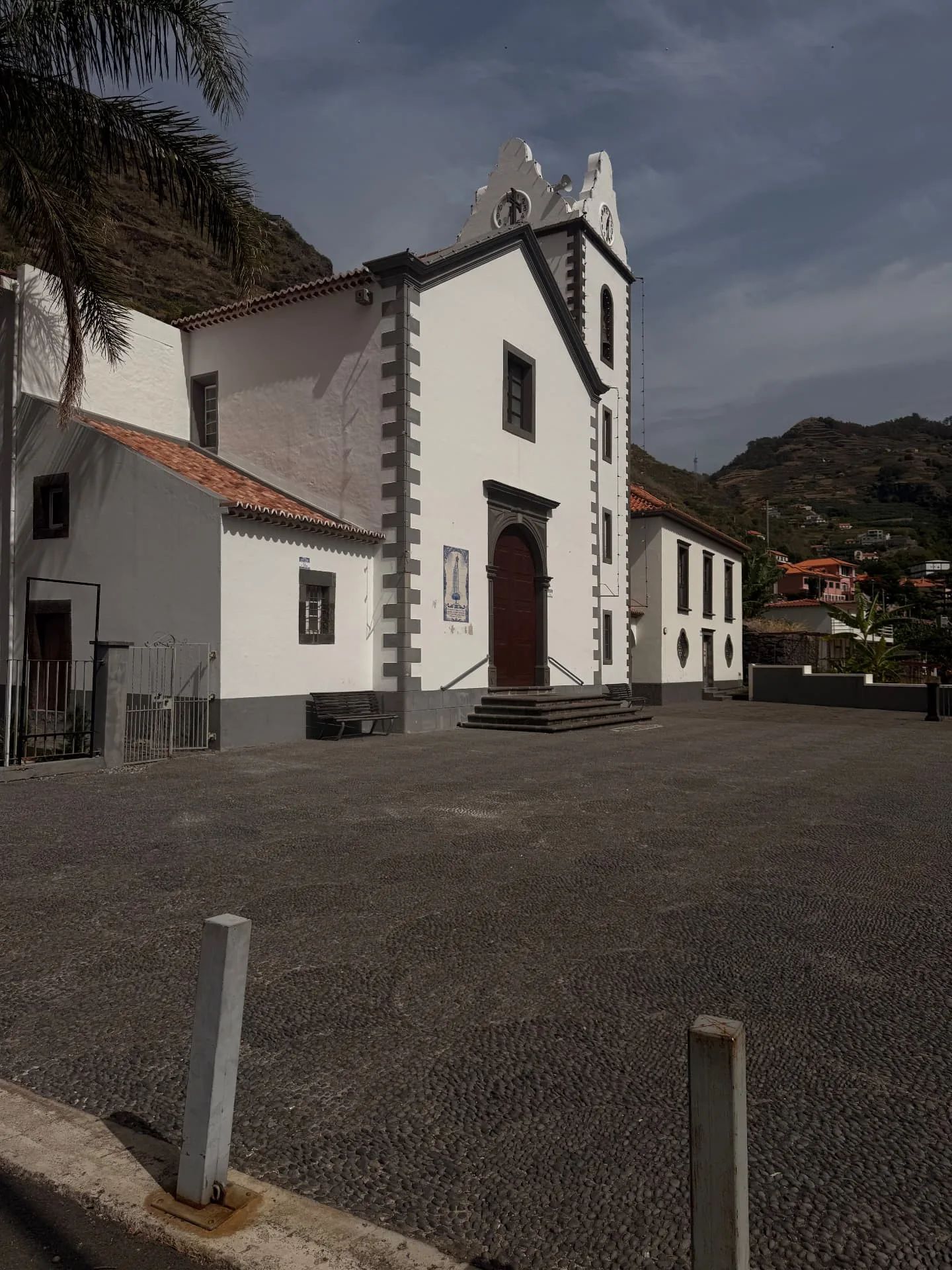 Fachada da igreja paroquial de Tabua, do outro lado da sua praça pavimentada com calçada de seixos