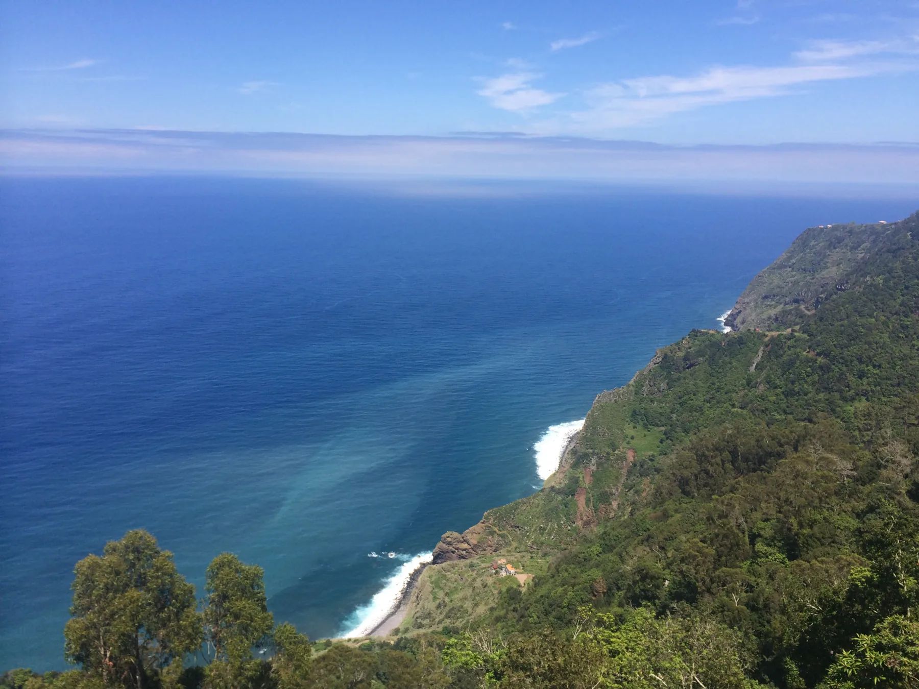 Sheer green cliffs dropping to a pebble shore seen from Miradouro das Cabanas