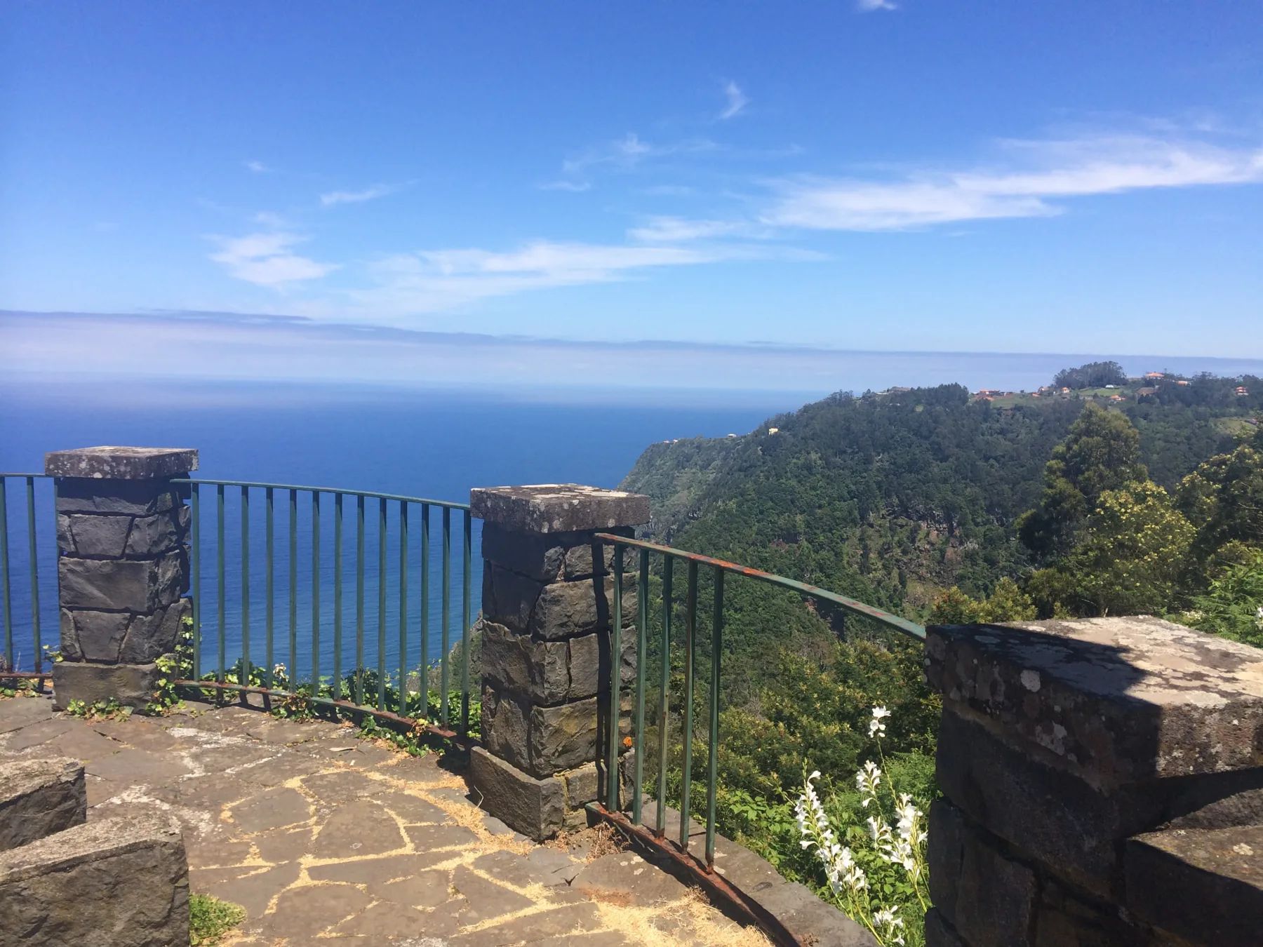 Stone pillars and railings above the sea and forested cliffs at Miradouro das Cabanas