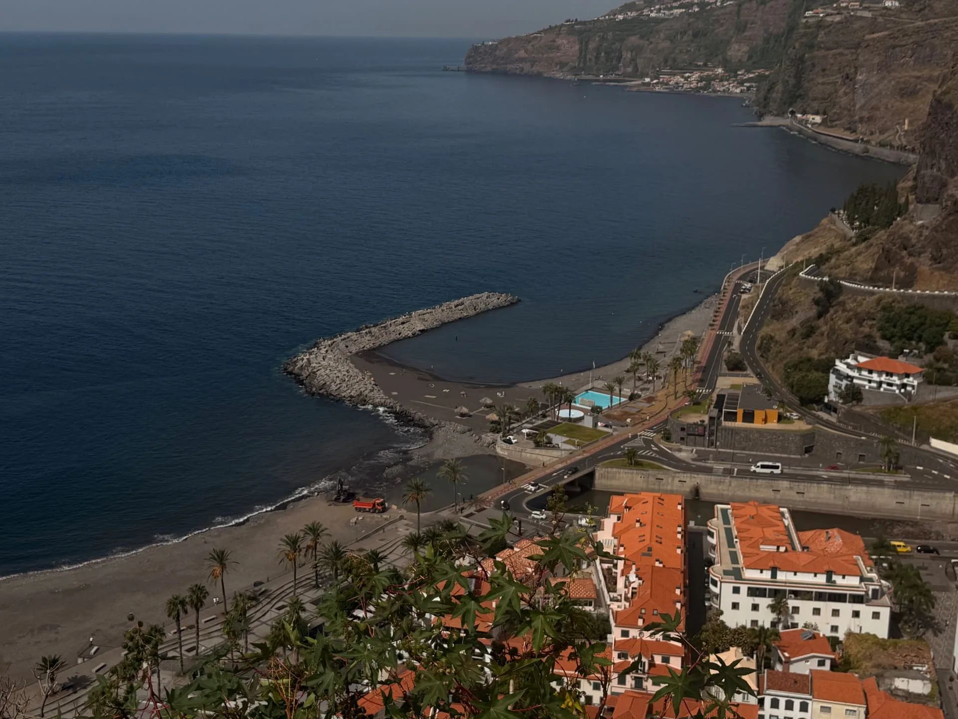 View from Miradouro de São Sebastião down onto Ribeira Brava beach, the breakwater, the seafront pool and the south coast cliffs