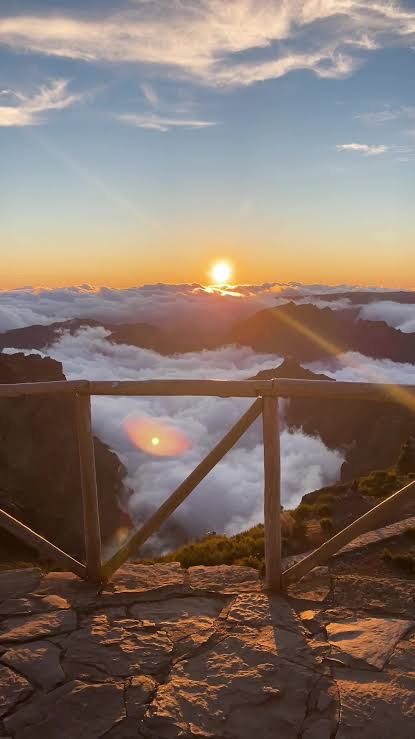 Wooden railing above cloud-filled mountain valleys with the sun low on the horizon